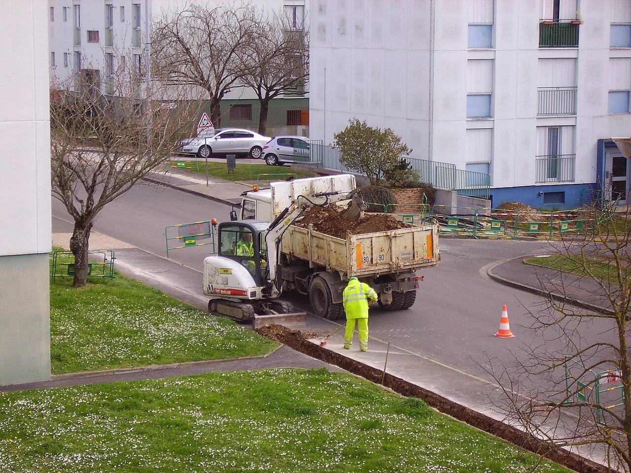 Compact excavator digging a narrow utility trench along a footpath