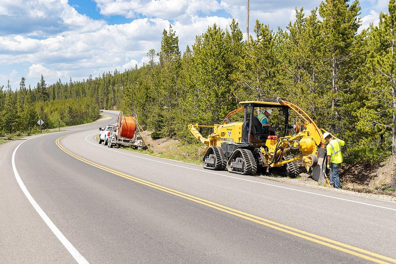 Crew laying fibre optic cable beside a highway with a tracked plough and cable drum