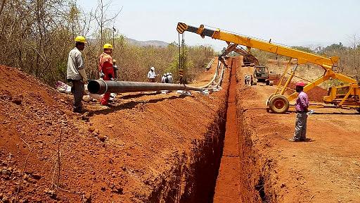 Crane lowering a pipe section into an open trench while the crew guides it into place